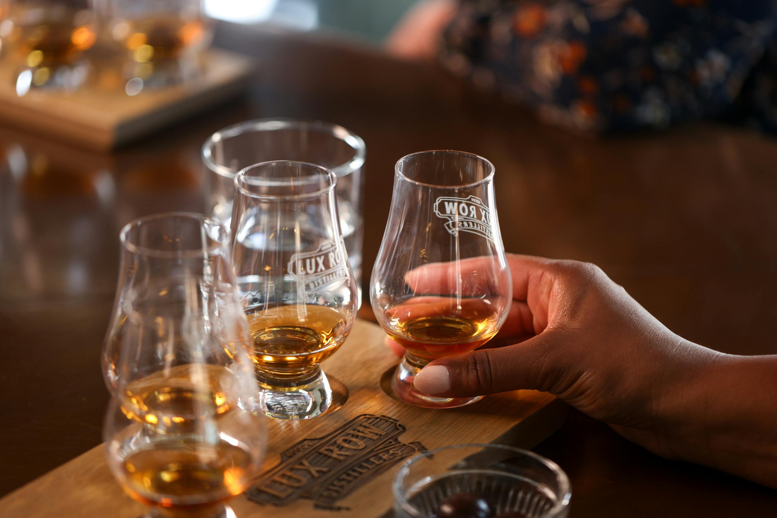 A set of glasses filled with bourbon samples, with a hand holding one.