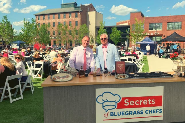 Kevin Harned and Tim Laird at the Paristown Oaks Garden Party, featuring a display for "Secrets of Bluegrass Chefs."