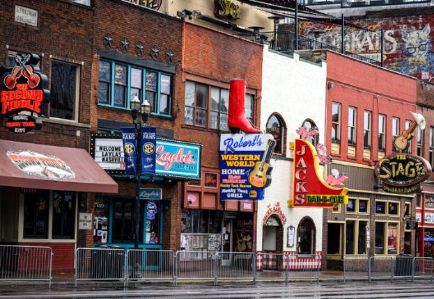 Bars and restaurants along Broadway in Nashville during the daytime, with storefronts and signs lining the street.