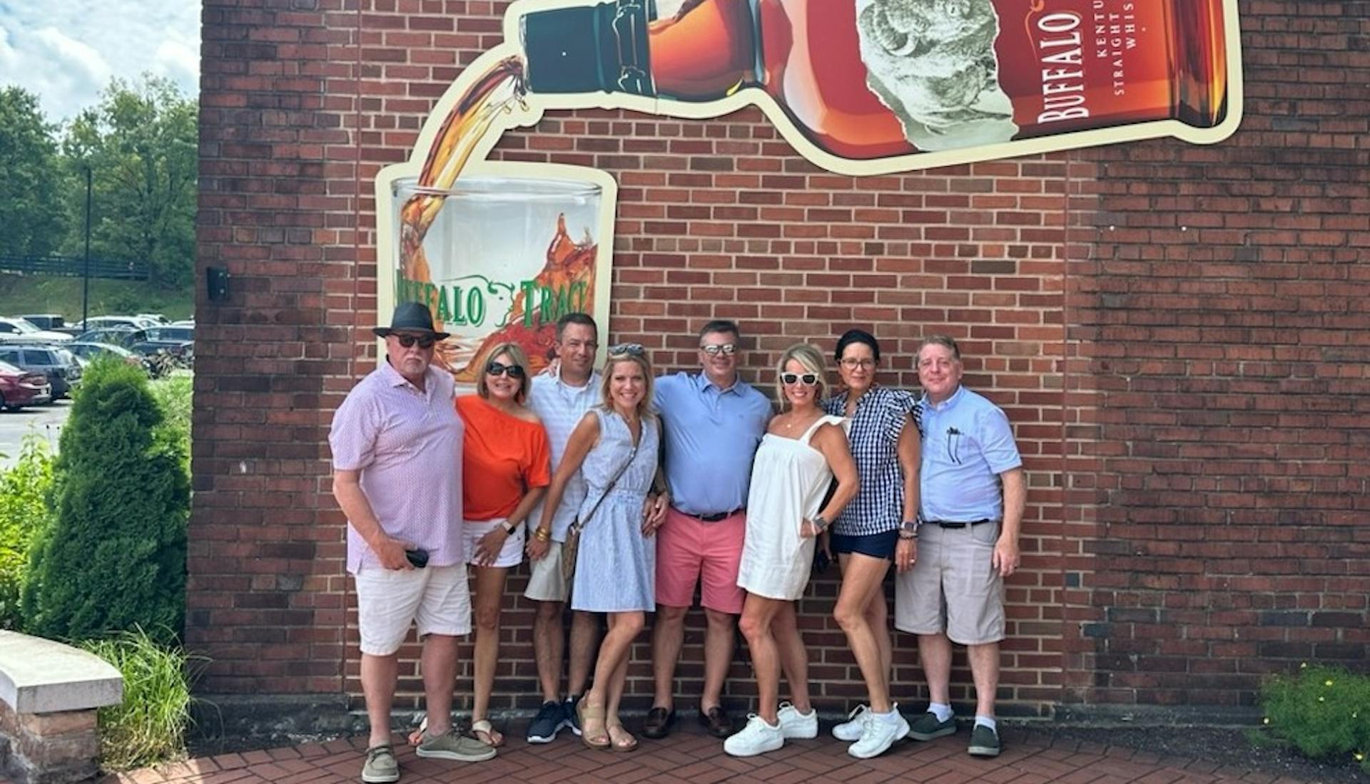 Group poses in front of the Buffalo Trace logo on a Buffalo Trace Tour.