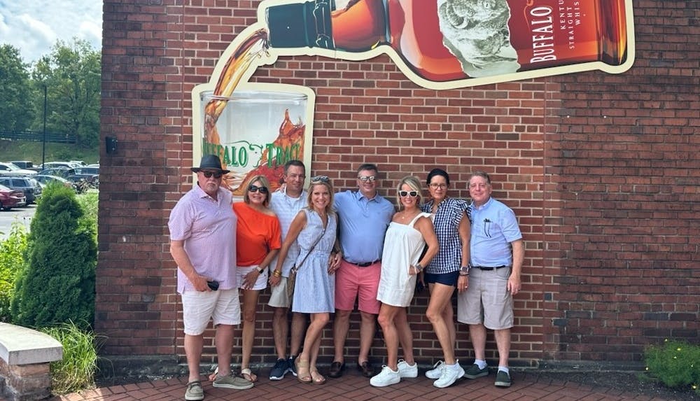 Group poses in front of the Buffalo Trace logo on a Buffalo Trace Tour.
