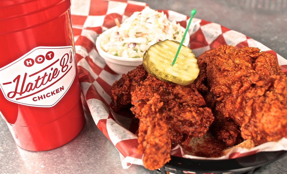 A plate of Hattie B's Hot Chicken served with a side of coleslaw and a drink.