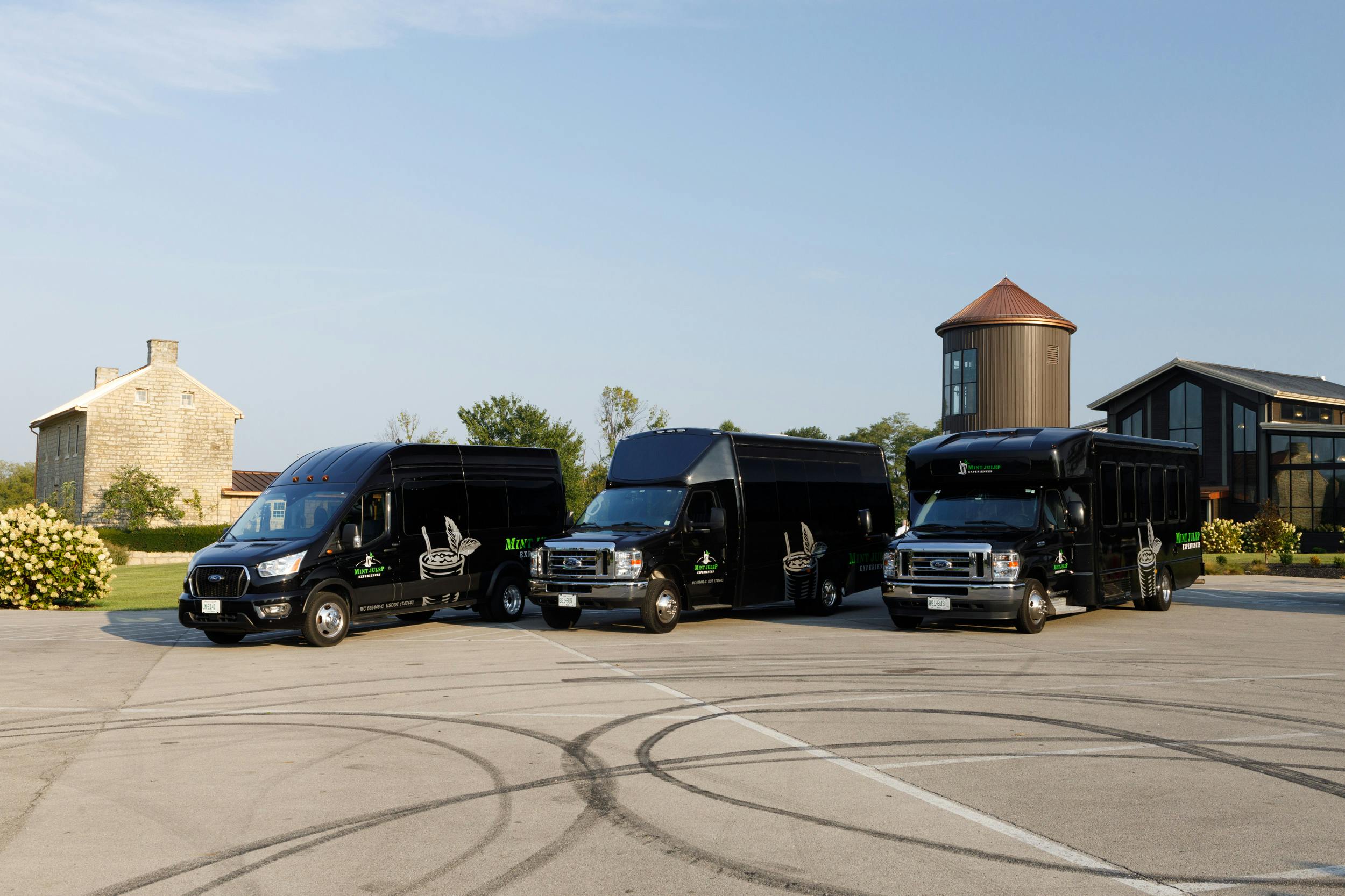 Three executive Mint Julep Experiences shuttles in front of a whiskey distillery.