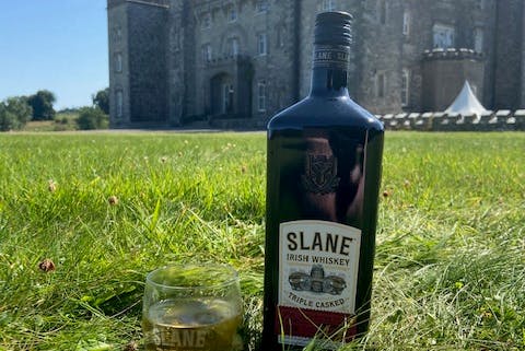 A bottle of Slane Irish Whiskey placed on the grass, with the iconic Slane Castle in the background.