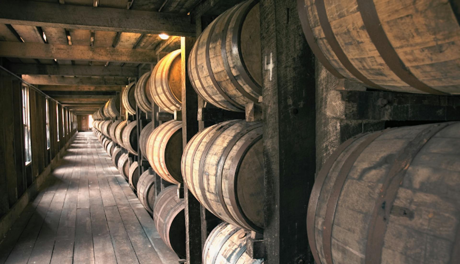 Rows of wooden barrels inside a rickhouse.