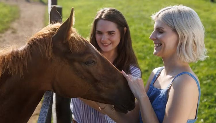 Two tourists on a Kentucky horse farm tour gently petting the head of a horse.