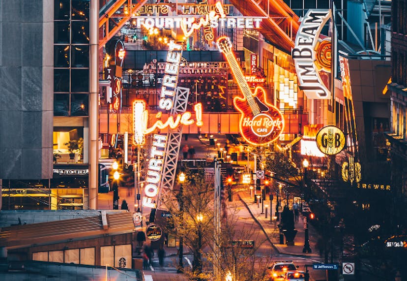 Fourth Street Live! in Louisville, KY, is illuminated by bright neon lights from various establishments, creating a lively and vibrant nightlife atmosphere.
