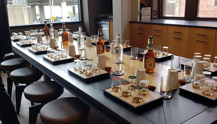 A large table with sets of drinking glasses, each containing samples of bourbon.
