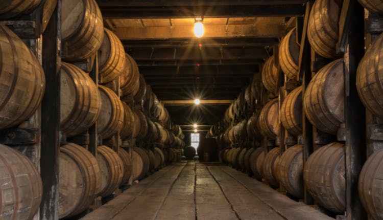 Rows of wooden bourbon barrels aging in a rickhouse.