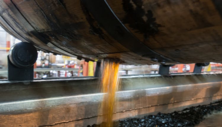 A wooden bourbon barrel with a hole on its side, draining liquid into a char filtration system below as part of the whiskey production process.