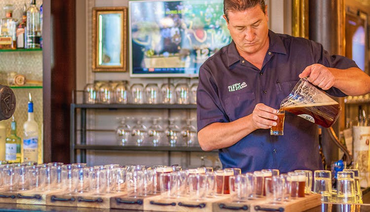 A man pouring a drink from a pitcher into glasses.