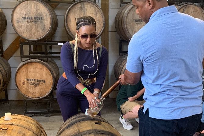 A woman engaged in a bourbon thieving experience, drawing whiskey directly from a barrel using a thief tool.