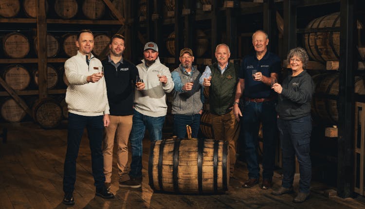Men holding out bourbon glasses inside a barrelhouse during the Bardstown Bourbon Collection Experience.