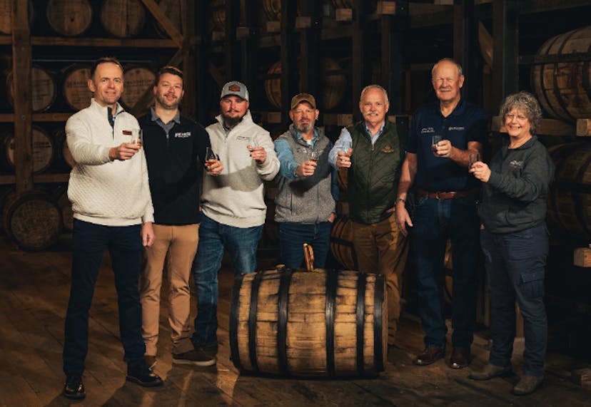 Men holding out bourbon glasses inside a barrelhouse during the Bardstown Bourbon Collection Experience.