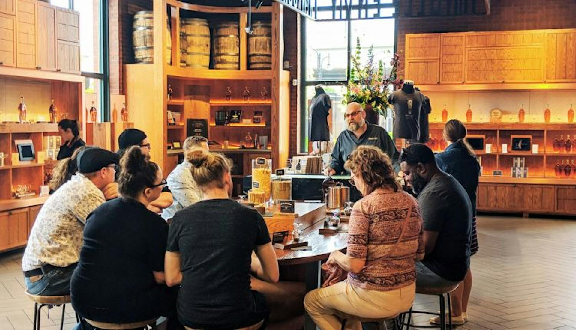 A group of people seated around a table at a distillery, participating in a bourbon tasting.