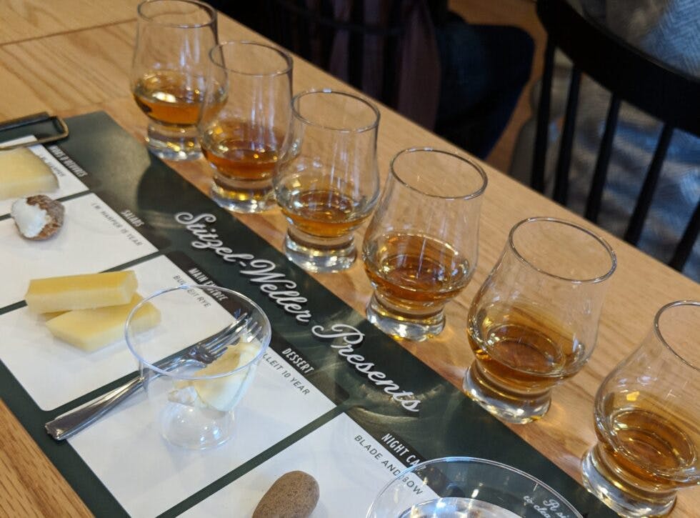 A table set for a bourbon and cheese tasting, featuring glasses of bourbon paired with a variety of cheeses.