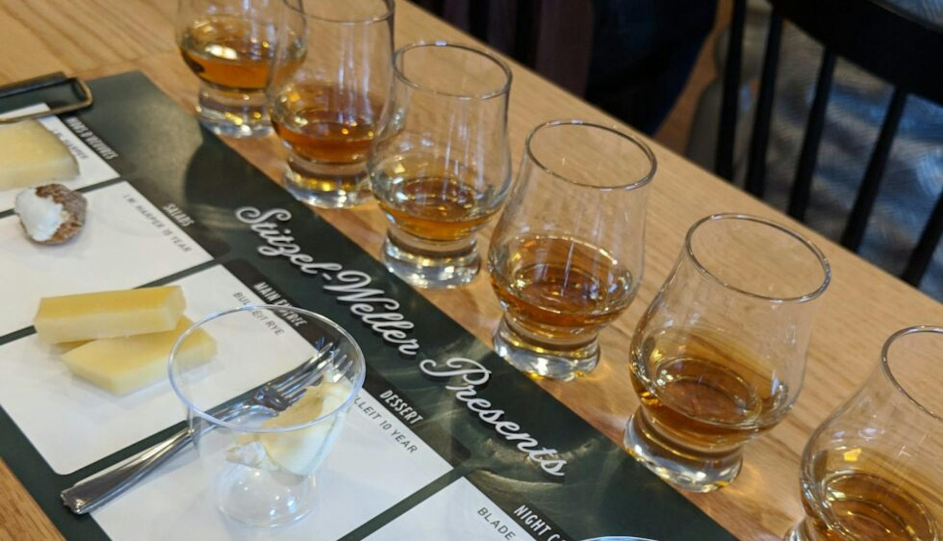A table set for a bourbon and cheese tasting, featuring glasses of bourbon paired with a variety of cheeses.