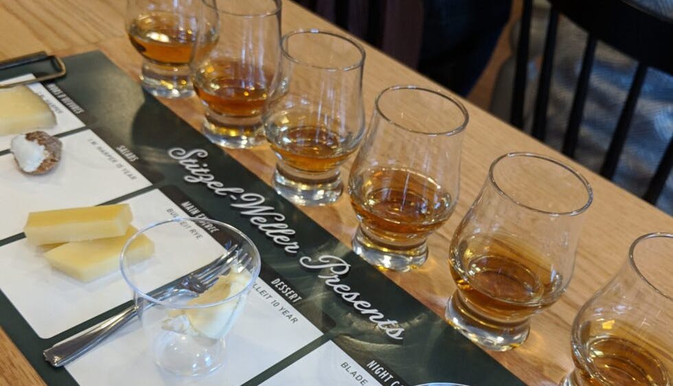A table set for a bourbon and cheese tasting, featuring glasses of bourbon paired with a variety of cheeses.