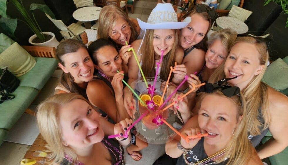 A group of women at a bachelorette party smiling and enjoying cocktails together.