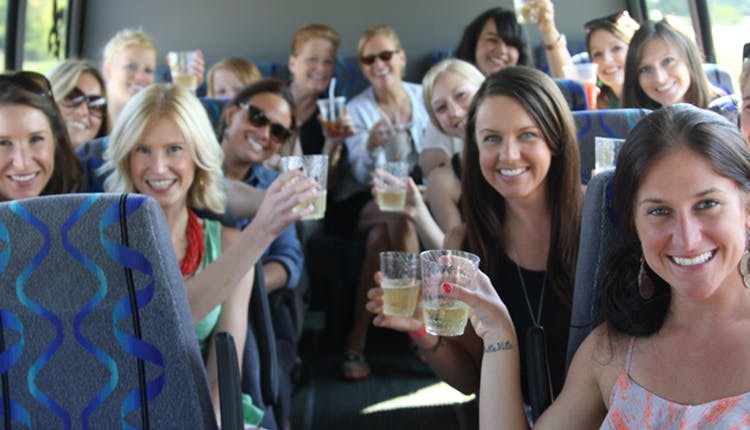 A group of women in a luxury tour vehicle, enjoying their Mint Julep Experiences whiskey tour, holding drinks and smiling as they pose for a photo.