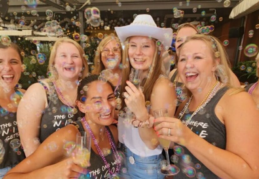A group of women at a bachelorette party, smiling and posing for the camera while holding  drinks, celebrating joyfully.