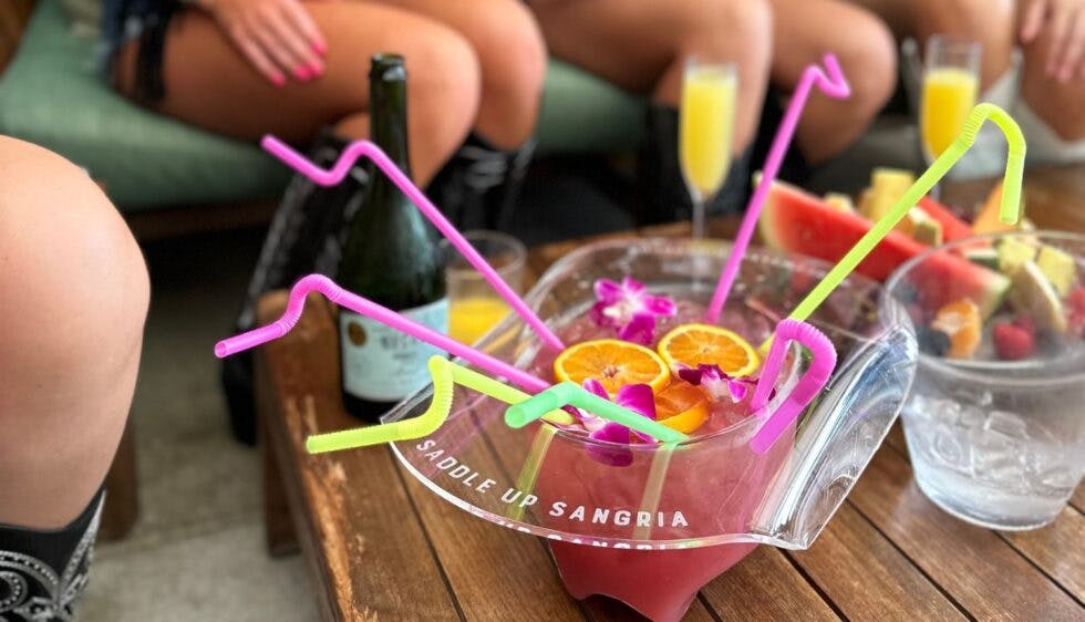 A cocktail served in a hat-shaped container, garnished with fruit slices and multiple colorful straws for a fun, festive presentation.