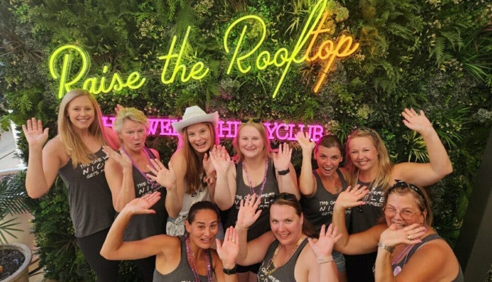 A group of women at a bachelorette party posing in front of the 'Raise the Rooftop' neon lights at The Twelve Thirty Club.