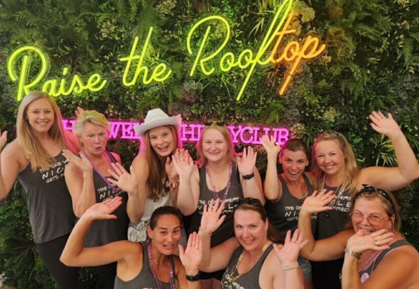 A group of women at a bachelorette party posing in front of the 'Raise the Rooftop' neon lights at The Twelve Thirty Club.