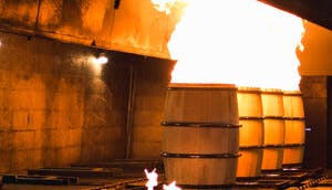 Several wooden barrels actively being charred by open flames during the barrel-making process.