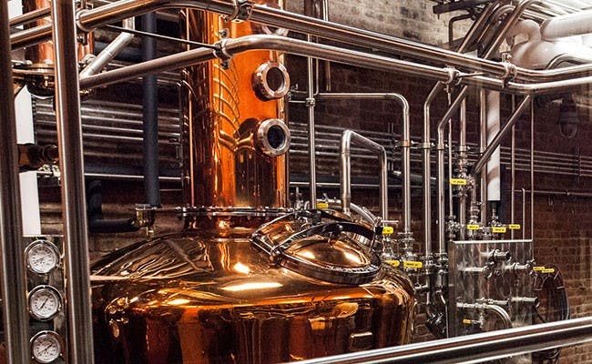 A large industrial copper still, prominently featured in a distillery setting.