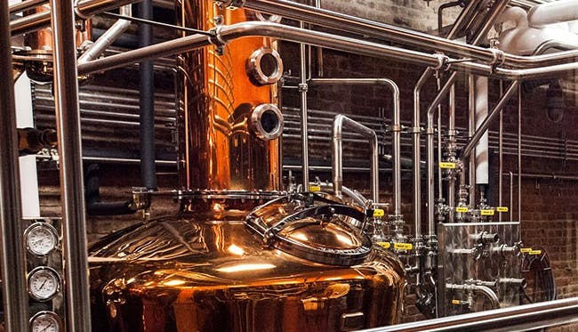 A large industrial copper still, prominently featured in a distillery setting.