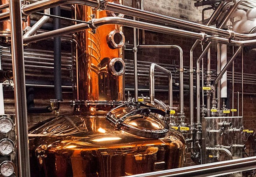 A large industrial copper still, prominently featured in a distillery setting.