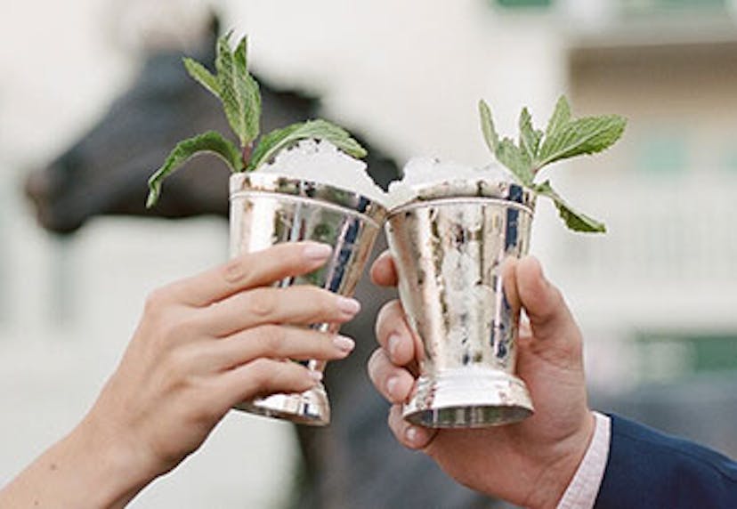 Two hands holding Mint Julep cocktails in silver cups, clinking together.