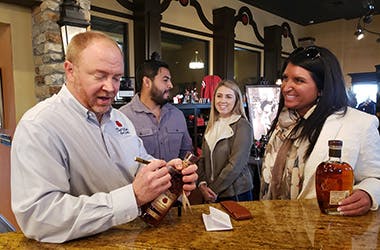 A master distiller at Four Roses Bourbon signing a bottle of bourbon, while guests stand nearby, waiting for their turn.