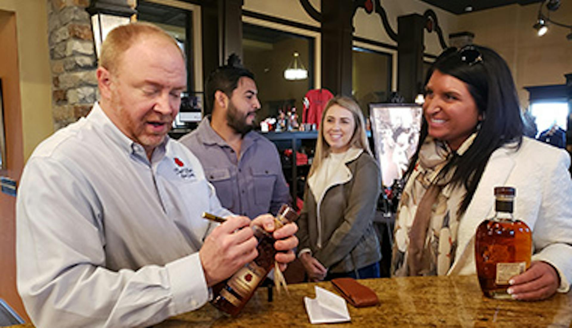 A master distiller at Four Roses Bourbon signing a bottle of bourbon, while guests stand nearby, waiting for their turn.