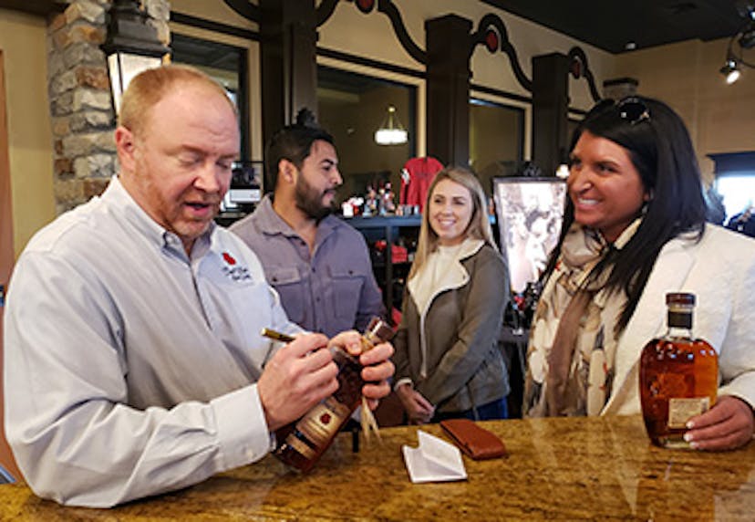 A master distiller at Four Roses Bourbon signing a bottle of bourbon, while guests stand nearby, waiting for their turn.