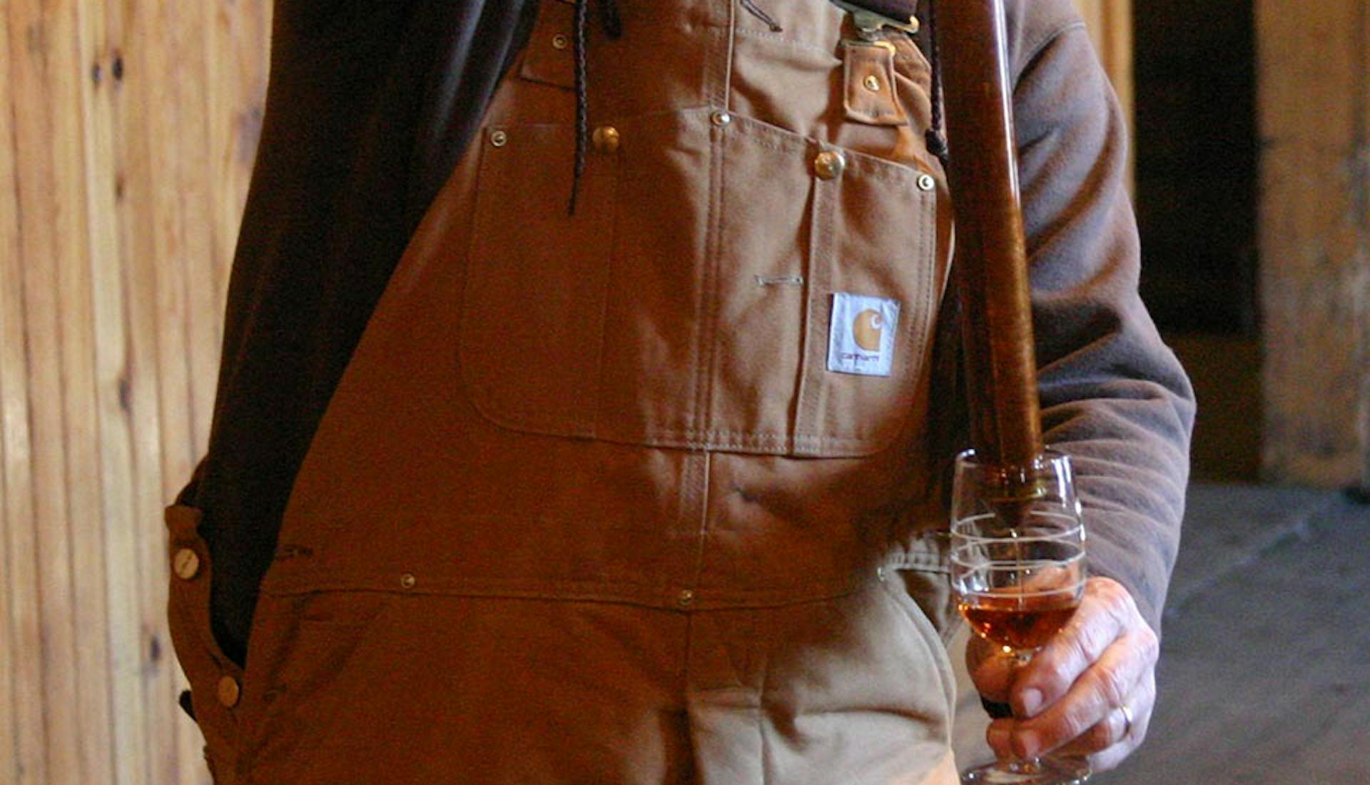 A man using a bourbon thief to pour a bourbon sample into a glass during a tasting experience.
