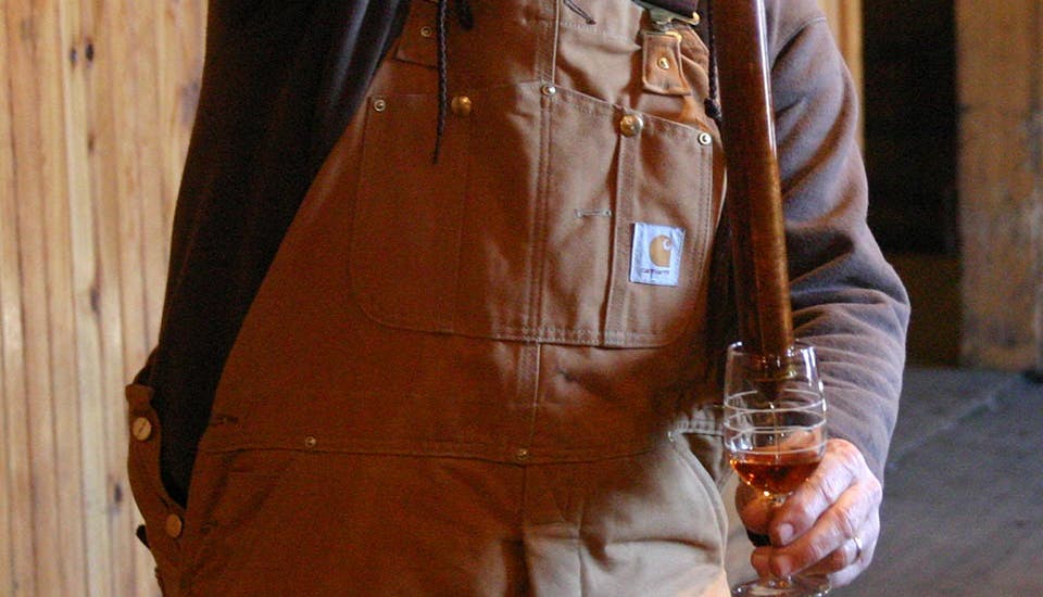 A man using a bourbon thief to pour a bourbon sample into a glass during a tasting experience.
