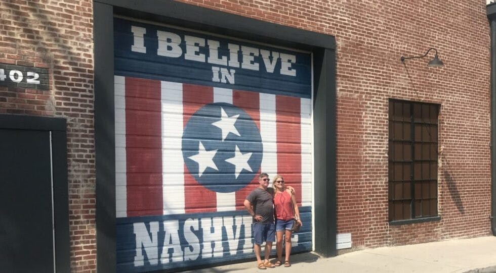 A couple posing in front of a mural that reads "I believe in Nashville."