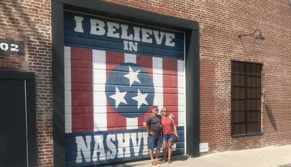 A couple posing in front of a mural that reads "I believe in Nashville."