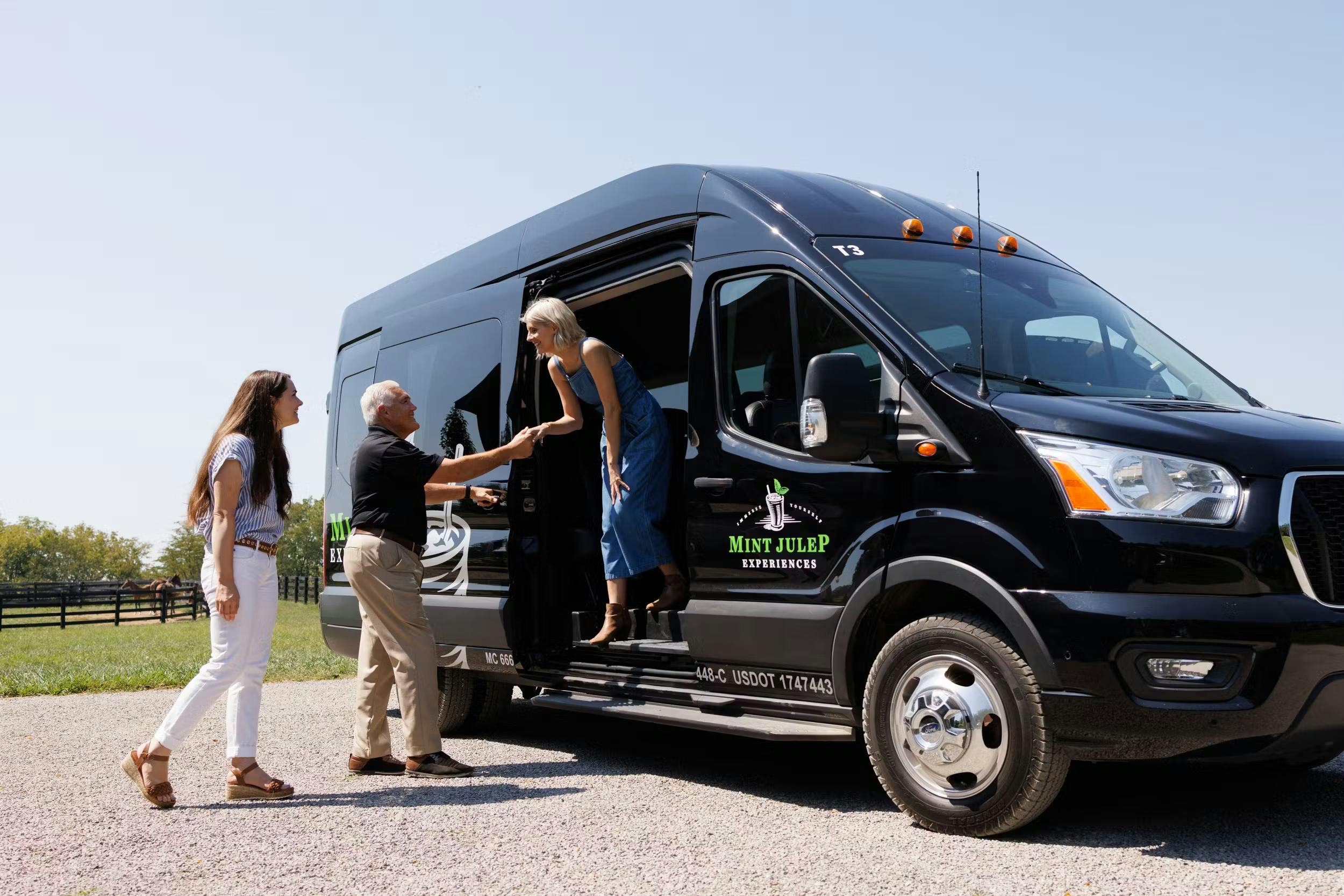 A lady stepping out of a black luxury tour vehicle, assisted by a Mint Julep Experiences staff member, while another tourist looks on.
