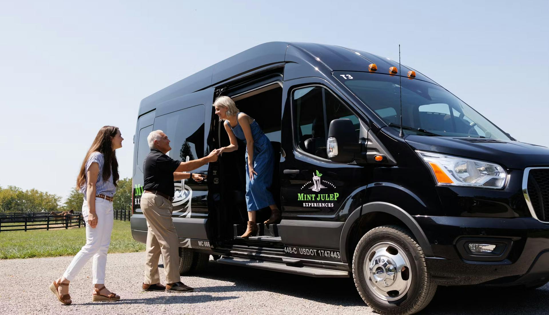 A lady stepping out of a black luxury tour vehicle, assisted by a Mint Julep Experiences staff member, while another tourist looks on.