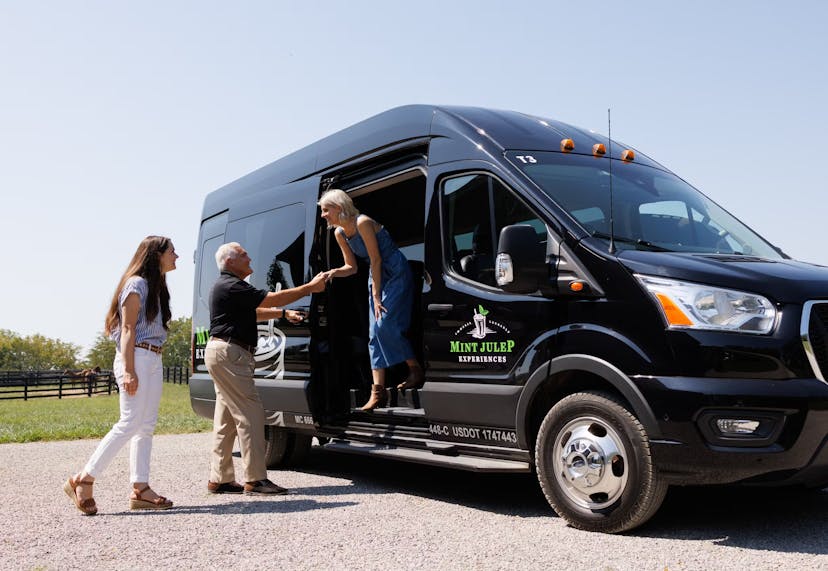 Guests exiting a luxury tour vehicle from Mint Julep Experiences, with assistance from a uniformed staff member.