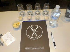 An Executive Bourbon Steward Workbook alongside whiskey glasses on a table at Moonshine University.