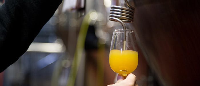 A glass being filled with craft beer directly from a tap installed on a wooden barrel at a brewery.