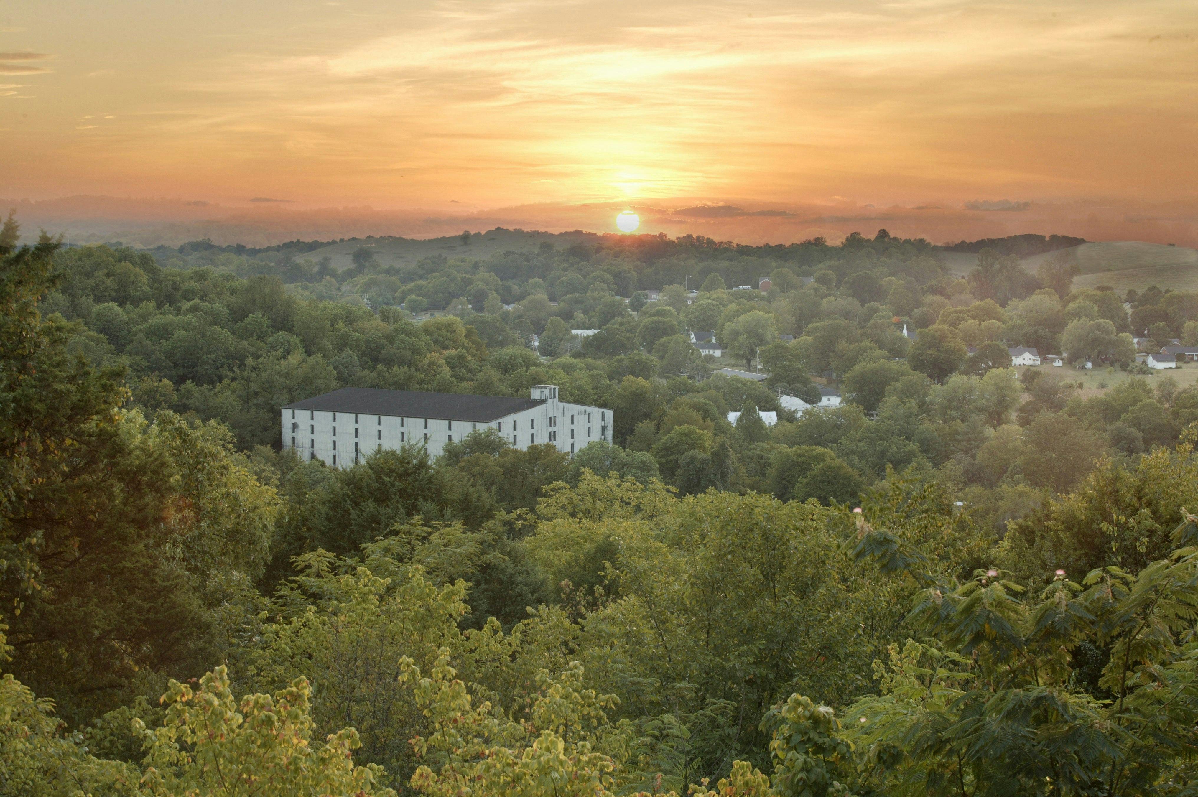 A large white barrelhouse surrounded by green trees at sunset in Lynchburg, Tennessee.