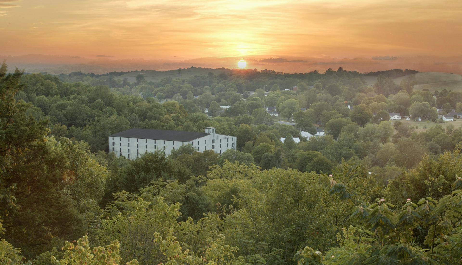 A large white barrelhouse surrounded by green trees at sunset in Lynchburg, Tennessee.