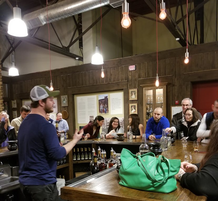 A whiskey tour at a rustic bar featuring a group of people listening to a guide behind the counter.A whiskey tasting event at a rustic bar featuring a group of people listening to a guide behind the counter.