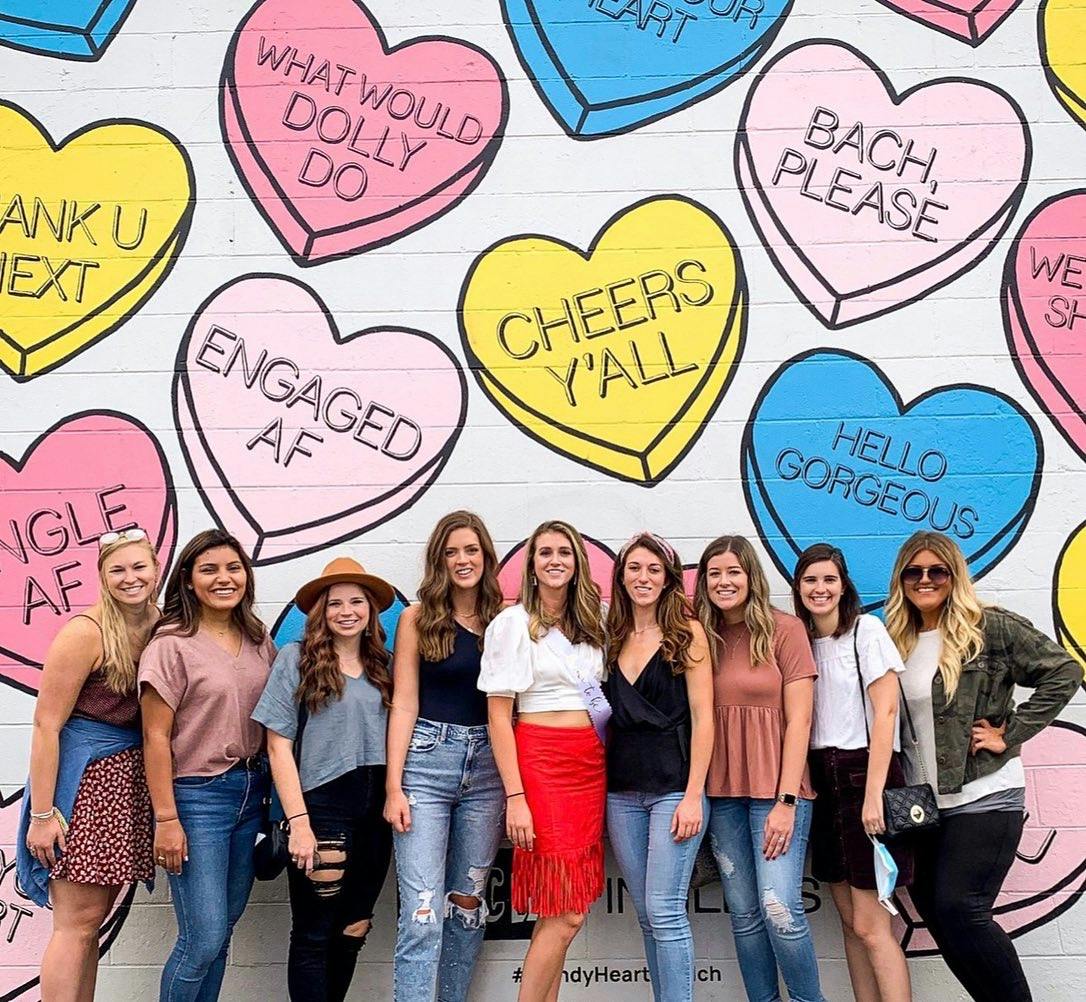Group of women posing in front of a colorful mural with candy heart phrases in Nashville.