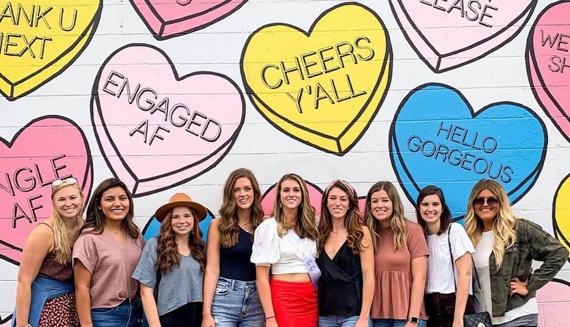 Group of women posing in front of a colorful mural with candy heart phrases in Nashville.